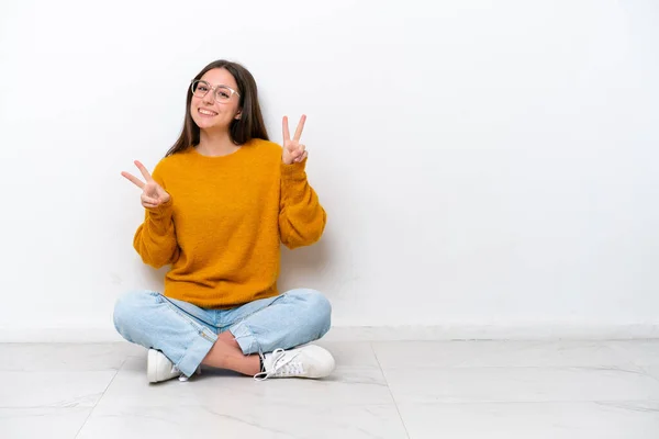 Mladá Dívka Sedí Podlaze Izolované Bílém Pozadí Ukazuje Vítězství Znamení — Stock fotografie