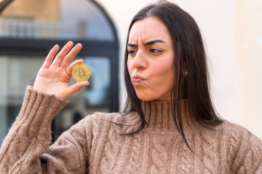 Dışarıda Bitcoin tutan genç bir kadın üzgün bir ifadeyle