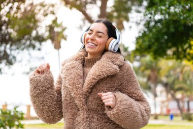 Genç esmer kadın açık havada müzik dinliyor ve dans ediyor.