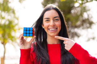 Genç bir kadın dışarıda üç boyutlu bir bulmaca küpünü tutuyor ve ona doğrultuyor.