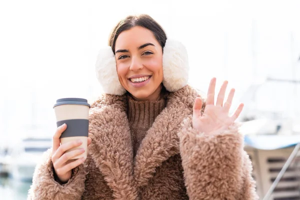年轻女子身穿冬衣 手持咖啡 带着愉快的表情在户外敬礼 — 图库照片
