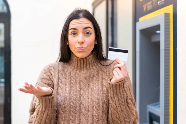 Młoda Kobieta Kartą Kredytową Świeżym Powietrzu Robi Wątpliwy Gest Podnosząc — Zdjęcie stockowe