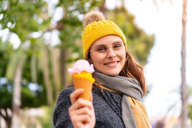 Açık havada kornet dondurmalı esmer bir kadın, neşeli bir ifadeyle.