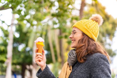 Açık havada kornet dondurmalı esmer bir kadın, neşeli bir ifadeyle.