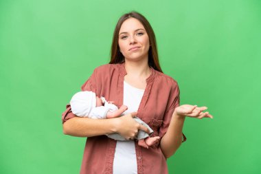 Yeni doğmuş bebeğiyle genç sarışın kadın izole edilmiş krom anahtar arkaplan üzerinde omuzlarını kaldırırken şüphe uyandıran hareketler yapıyor.