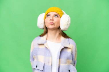 Sarışın genç bir kadın izole edilmiş krom arka planda kışlık manşetler takıyor ve yukarı bakıyor.