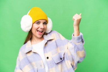 Sarışın genç bir kadın, krom arka planda kışlık manşetler takıyor gitar hareketi yapıyor.