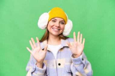 İzole edilmiş krom arka plan üzerinde kışlık manşet takan genç sarışın kadın parmaklarıyla on tane sayıyor.