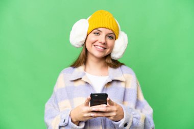 İzole edilmiş krom anahtar arkaplan üzerine kış maskesi takan genç sarışın kadın cep telefonuyla bir mesaj gönderiyor.