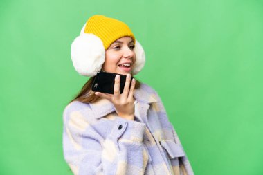 İzole edilmiş krom anahtar geçmişi olan, kış maskesi takan genç sarışın bir kadın cep telefonuyla sohbet ediyor.