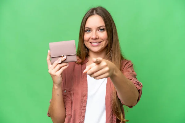 Young blonde woman holding a wallet over isolated chroma key background points finger at you with a confident expression