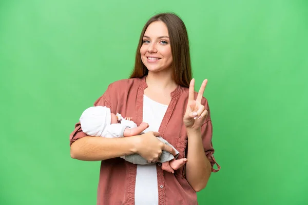 若いですブロンド女性とともに彼女の新生児上の隔離されたクロマキーバック笑顔とショー勝利サイン — ストック写真