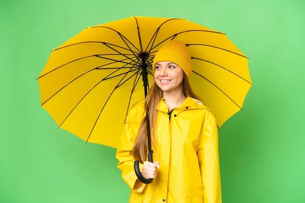 若いですブロンド女性とともにレインプルーフコートと傘上の隔離されたクロマキー背景見て側 — ストック写真