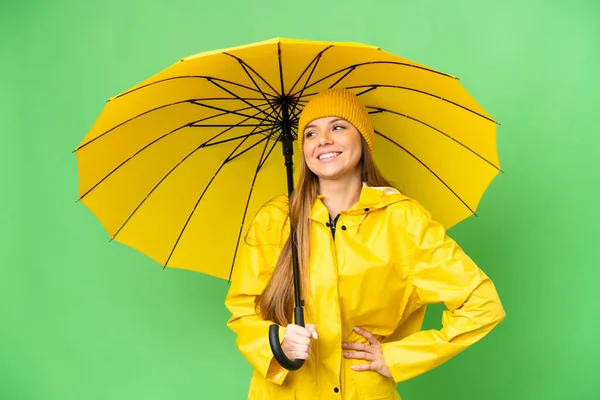 若いですブロンド女性とともにレインプルーフコートと傘上の隔離されたクロマキーバックポーズアームで尻と笑顔 — ストック写真