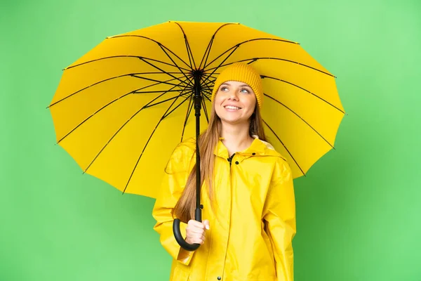 若いですブロンド女性とともにレインプルーフコートと傘上の隔離されたクロマキー背景考えますAアイデアながら見上げます — ストック写真
