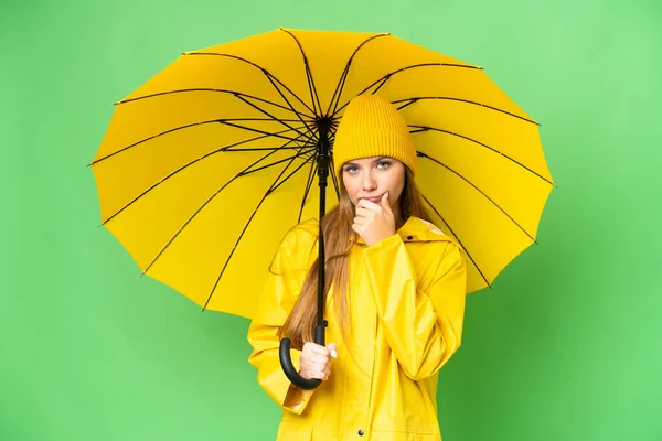 若いですブロンド女性とともにレインプルーフコートと傘上の隔離されたクロマキー背景思考 — ストック写真