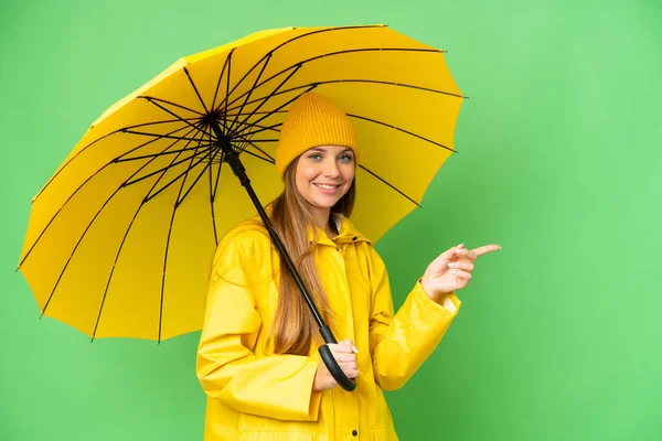 若いですブロンド女性とともにレインプルーフコートと傘上の隔離されたクロマキー背景指摘指へザ側 — ストック写真