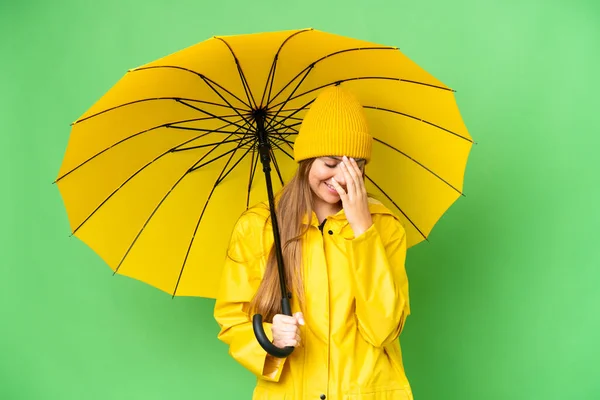 若いですブロンド女性とともにレインプルーフコートと傘上の隔離されたクロマキー背景笑い — ストック写真