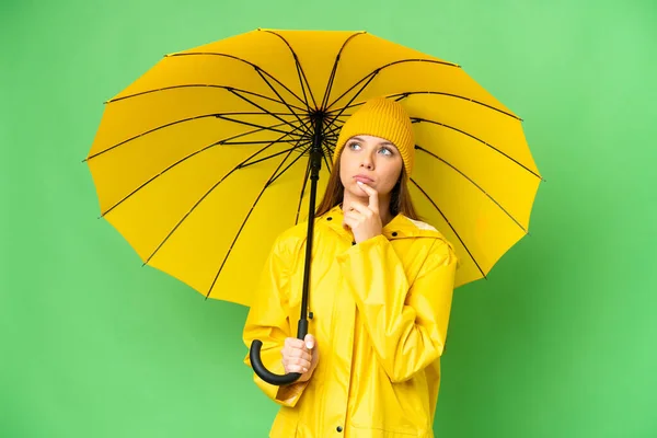 若いですブロンド女性とともにレインプルーフコートと傘上の隔離されたクロマキー背景と見上げます — ストック写真