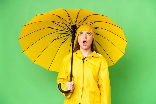 若いですブロンド女性とともにレインプルーフコートと傘上の隔離されたクロマキーバック検索アップと驚きの表情 — ストック写真