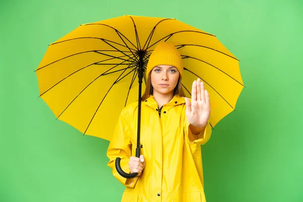 若いですブロンド女性とともにレインプルーフコートと傘上の隔離されたクロマキー背景メイキングストップジェスチャー — ストック写真