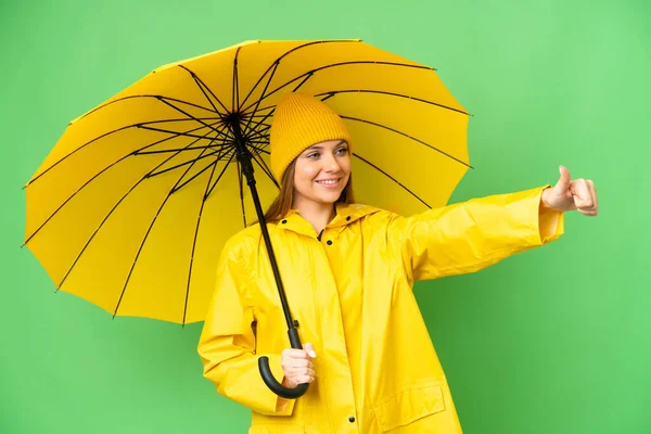 若いですブロンド女性とともにレインプルーフコートと傘上の隔離されたクロマキー背景与えます親指アップジェスチャー — ストック写真