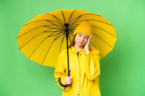 若いですブロンド女性とともにレインプルーフコートと傘上の隔離されたクロマキー背景とともに頭痛 — ストック写真