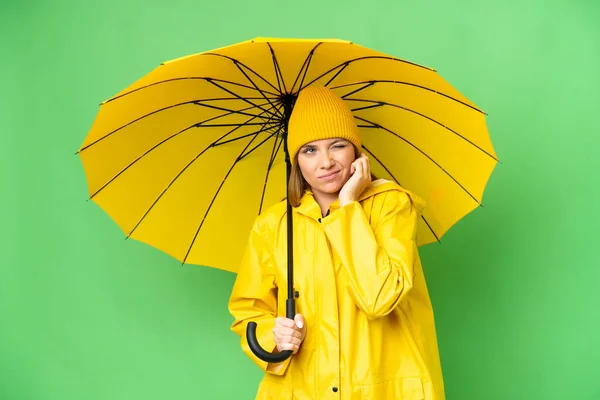若いですブロンド女性とともにレインプルーフコートと傘上の隔離されたクロマキーバックフラストレーションとカバー耳 — ストック写真