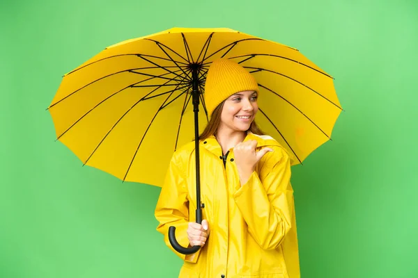 若いですブロンド女性とともにレインプルーフコートと傘上の隔離されたクロマキー背景を指す側に製品を提示 — ストック写真