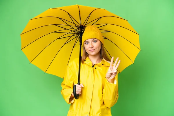 若いですブロンド女性とともにレインプルーフコートと傘上の隔離されたクロマキー背景幸せとカウント3とともに指 — ストック写真