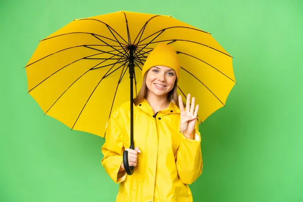 若いですブロンド女性とともにレインプルーフコートと傘上の隔離されたクロマキー背景幸せとカウント4とともに指 — ストック写真