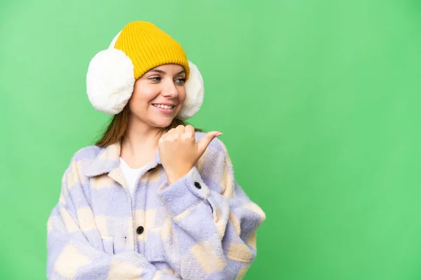 年轻的金发女郎披着冬衣 披着孤立的彩色关键背景 指着侧面展示自己的产品 — 图库照片
