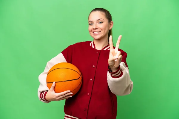 若いですブロンド女性遊びバスケットボール上の隔離されたクロマキー背景笑顔とショー勝利サイン — ストック写真