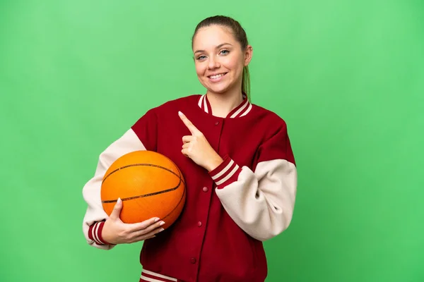Молодая Блондинка Играющая Баскетбол Над Изолированным Цветовым Фоном Указывая Сторону — стоковое фото