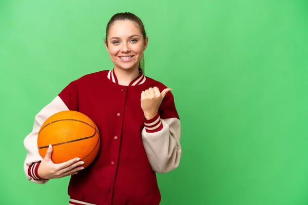 若いですブロンド女性プレイバスケットボール上の隔離されたクロマキー背景を指す側に製品を提示 — ストック写真
