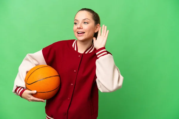 Młoda Blondynka Gra Koszykówkę Odizolowanym Tle Chroma Key Słuchając Czegoś — Zdjęcie stockowe