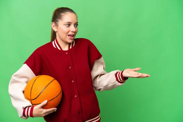 年轻的金发女子一边看着旁边一边用惊讶的表情在孤立的彩色关键背景上打篮球 — 图库照片