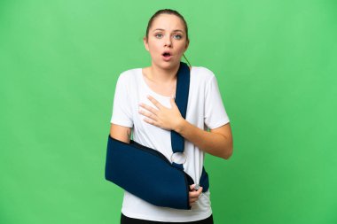 Kırık kollu genç sarışın kadın ve izole edilmiş krom anahtar üzerine askı takıyor sağa bakarken şaşırmış ve şok olmuş.