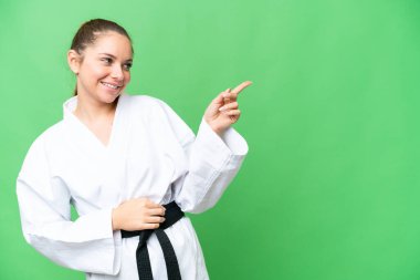 Karate yapan genç sarışın kadın izole edilmiş krom arka plan üzerinde parmak göstererek bir ürün sunuyor.