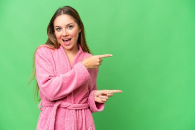 Bornozlu genç bir kadın izole edilmiş krom anahtar arka planı şaşırmış ve işaret ediyor.