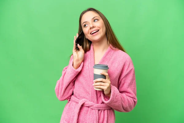 一个穿着浴衣的年轻女人 在与外界隔绝的有色人种背景下 手里拿着咖啡和手机 — 图库照片
