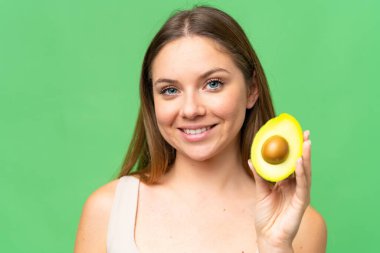 Sarışın, izole edilmiş arka planı olan genç bir kadın elinde avakado tutarken gülümsüyor. Portreyi kapat