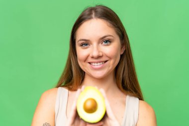 Sarışın, izole edilmiş arka planı olan genç bir kadın elinde avakado tutarken gülümsüyor. Portreyi kapat