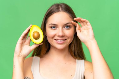 Sarışın, izole edilmiş arka planı olan genç bir kadın elinde avakado tutarken gülümsüyor. Portreyi kapat
