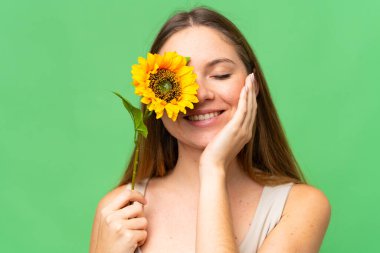 Sarışın, izole edilmiş arka planı olan genç bir kadın gülümserken elinde bir ayçiçeği tutuyor. Portreyi kapat