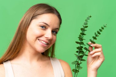 Sarışın, izole edilmiş, anahtar arka planı olan genç bir kadın elinde okaliptüs dalını tutarken gülümsüyor. Portreyi kapat