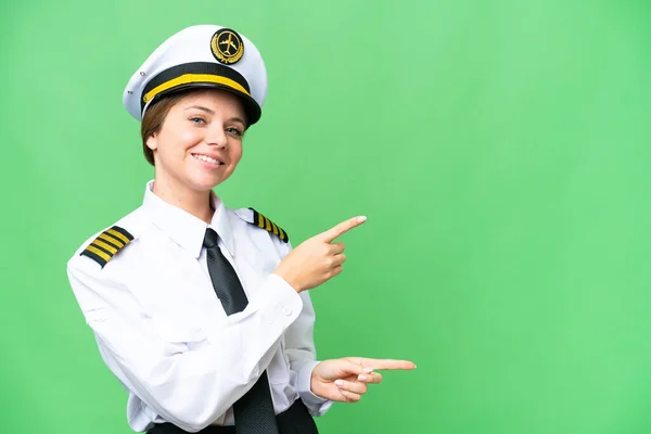 Airplane pilot woman over isolated chroma key background pointing finger to the side and presenting a product