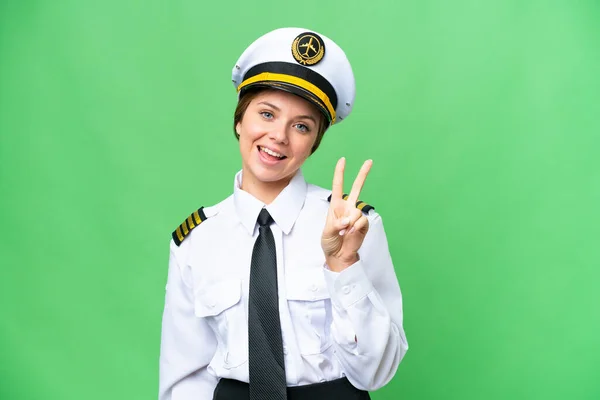 Airplane pilot woman over isolated chroma key background smiling and showing victory sign
