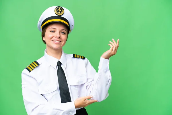 Airplane pilot woman over isolated chroma key background extending hands to the side for inviting to come