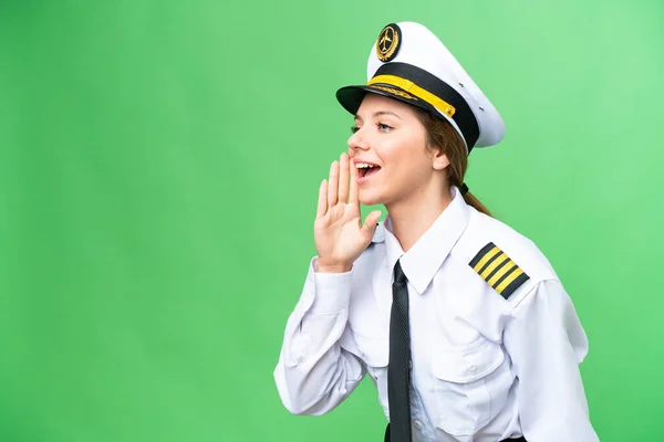 Airplane pilot woman over isolated chroma key background shouting with mouth wide open to the lateral